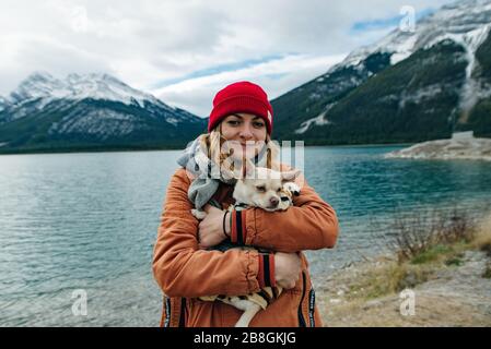 une fille dans une veste orange tient une chihuahua dans ses bras près du lac, au canada Banque D'Images