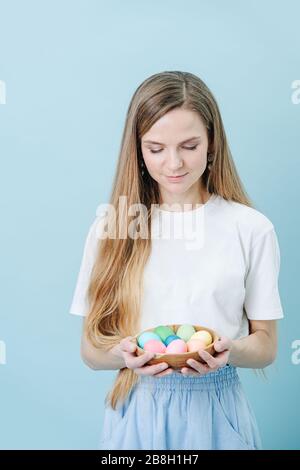 Heureuse femme heureuse regardant un bol d'œufs de pâques dans ses mains sur bleu Banque D'Images