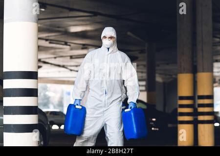 Homme dans une combinaison de protection contre le virus tenant deux jerrycans avec antiseptique Banque D'Images