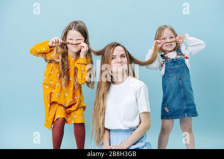 Les filles jouant avec les cheveux de leur mère font la moustache de cheveux sur bleu Banque D'Images