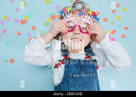 Happy Little girl se trouve sur un étage, tenant sur ses lunettes d'anniversaire Banque D'Images