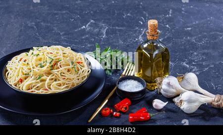 Pâtes Aglio, Olio e Peperoncino, spaghetti italien à l'ail, piment et huile d'olive dans un bol noir avec fourchette dorée et ingrédients sur un contr Banque D'Images