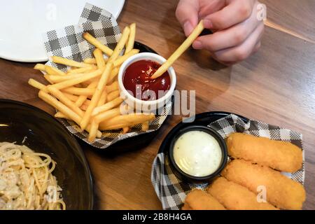 Main avec friture française fraîche trempée dans la sauce tomate, bâtonnets de poisson frits sur la table. Repas, déjeuner. Vue du dessus. Banque D'Images