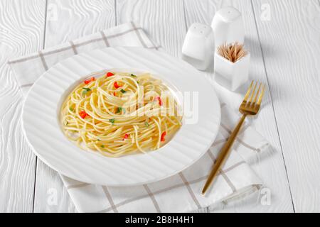 Gros plan de Pasta Aglio, Olio e Peperoncino, spaghetti italien à l'ail, au piment et à l'huile d'olive sur une plaque blanche avec fourchette dorée sur un t en bois Banque D'Images