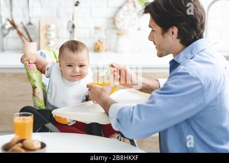 Papa nourrissant son bébé avec une nourriture saine et peu savoureuse Banque D'Images