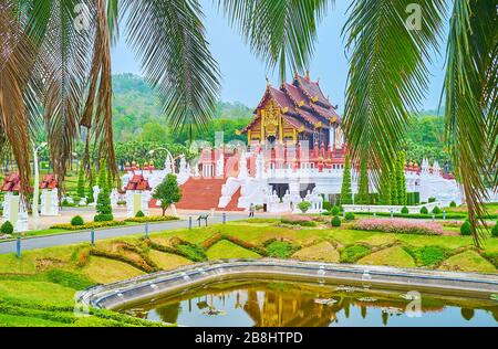 La vue sur le magnifique Pavillon Royal, entouré d'escaliers rouges et de sculptures blanches, à travers les branches verdoyantes de palmiers, le parc Rajarouek, Chian Banque D'Images