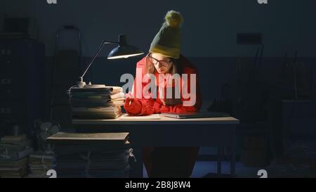 Femme d'affaires travaillant tard dans la nuit au bureau et verglaçante, elle porte un chapeau de laine et un manteau Banque D'Images