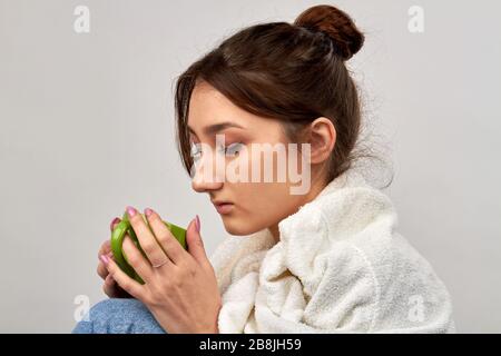 La jeune femme boit du thé chaud tout en ayant des symptômes de rhume et de grippe. Banque D'Images