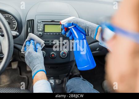 Le professionnel du lavage de voiture porte des gants de protection et désinfecte le tableau de bord de voiture avec un spray désinfectant et un chiffon. Banque D'Images