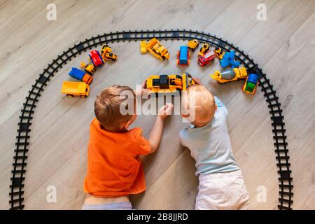 Les garçons d'âge préscolaire s'étirent sur papier, jouant avec des jouets éducatifs - blocs, train, chemin de fer, véhicules à la maison ou garderie. Jouets pour les enfants d'âge préscolaire et Banque D'Images