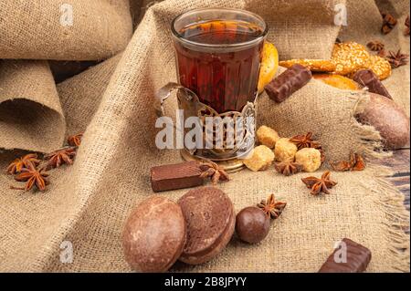 Un verre à facettes de thé dans un porte-gobelet millésime, des biscuits, des gâteaux au chocolat et du chocolat sur fond de tissu texturé. Gros plan Banque D'Images
