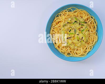 Spaghetti avec une sauce crème avec courgettes et poireaux dans une assiette bleu clair sur fond blanc d'en haut. Banque D'Images