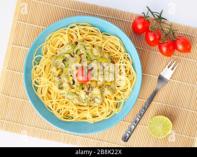 Spaghetti avec une sauce crème avec courgettes et poireaux avec quelques tomates pour la décoration dans une assiette bleu clair sur un fond blanc d'en haut. Banque D'Images