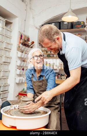 Senior woman spinning clay sur une roue avec une aide d'un professeur de classe de poterie Banque D'Images