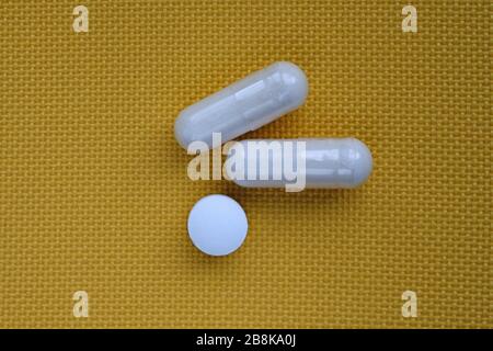 Arrondir la petite pilule blanche et deux capsules sur un fond jaune. Pilules, suppléments alimentaires vue de dessus. Banque D'Images
