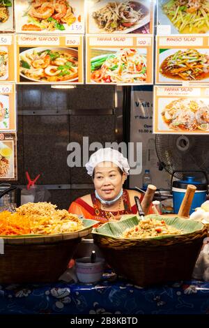 Chef local cuisine et vente de nourriture de rue de son stand, avec des photos de la nourriture disponible, dans le marché de la nourriture à Bangkok, Thaïlande Banque D'Images