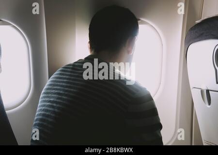Vue arrière d'un homme assis dans un avion, en regardant la vue depuis la fenêtre de l'avion. Banque D'Images