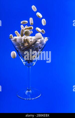 Chute de pilules blanches, comprimés capsule dans un verre de martini sur le dos bleu. Concept anti-gravité Banque D'Images