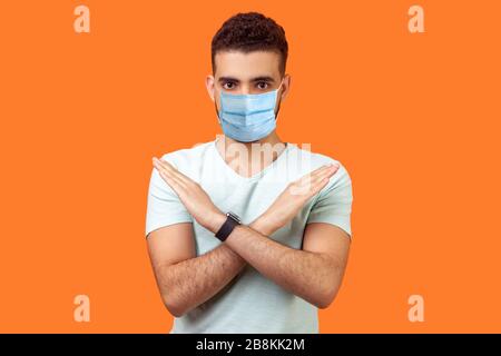 Pas du tout, absolument pas. Portrait de l'homme déterminé avec masque médical dans un t-shirt blanc montrant x signe avec des mains croisées, signifiant arrêt, c'est la fin Banque D'Images