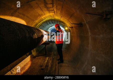 Le travailleur du tunnel examine le pipeline dans le tunnel souterrain. Banque D'Images