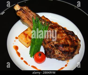 côtes de bœuf angus grillées avec pomme de terre, haricots verts et tomate dans une assiette blanche et noire Banque D'Images