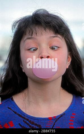 Une jeune fille qui croise ses yeux et souffle de la gomme de bulle, tout en faisant un visage drôle Banque D'Images