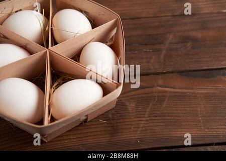 Les œufs blancs de poulet se trouvent dans un panier rond en bois qui se dresse sur une table en bois sombre. Fond de Pâques. Appartement de vacances saisonnier avec espace libre pour te Banque D'Images