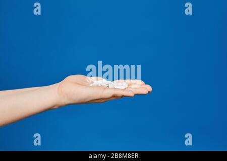 Pilules blanches sur une paume femelle ouverte étirée sur le côté gauche de la photo, isolée en fond bleu. Médicaments pour le virus et la grippe. Saisonnier Banque D'Images