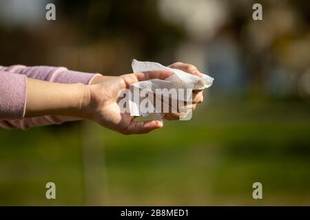 Nettoyer les mains avec des lingettes antibactériennes humides en plein air contre l'infection de la maladie par rapport à la grippe ou infuliza, fond vert flou Banque D'Images