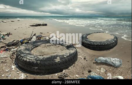 Les pneus de voiture et les bouteilles en plastique polluent dans une flaque boueuse sur la plage. (Concept d'environnement) Banque D'Images