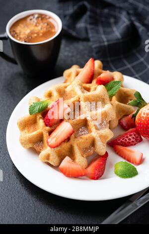 Gaufres belges avec fraises et sucre et tasse de café expresso sur fond noir Banque D'Images