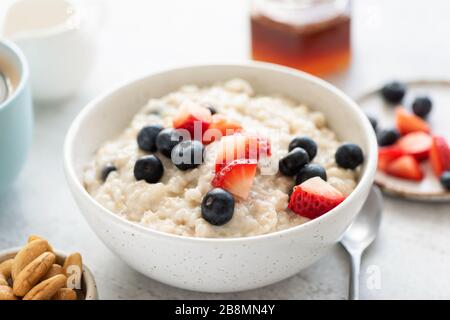 Porridge de flocons d'avoine avec fraises et bleuets dans un bol en céramique blanc vue rapprochée. Un petit déjeuner sain. Flocons d'avoine végétariens frais Banque D'Images