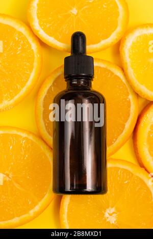 Huile essentielle aux agrumes, sérum de vitamine C, thérapie aromatique pour soins de beauté. Sérum naturel de vitamine C, soins de la peau, produits pétroliers essentiels. Flacon en verre brun cosmétique avec compte-gouttes et tranche de fruits orange frais juteux sur fond orange. Banque D'Images