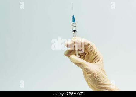 La main du médecin dans un gant en caoutchouc blanc contient une seringue médicale sur un fond bleu. Le concept de médecine et de soins médicaux pour le patient. Banque D'Images