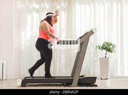 Photo de profil pleine longueur d'une femme en surpoids fatiguée exerçant sur un tapis roulant à la maison Banque D'Images