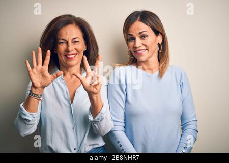 Beau couple de sœurs d'âge moyen debout sur fond blanc isolé montrant et pointant vers le haut avec les doigts numéro huit tout en souriant confide Banque D'Images