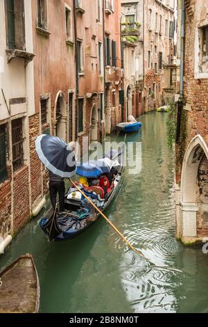 Gondolier naviguant sur les canaux de Venise avec des passagers sous la pluie. Banque D'Images