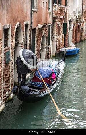 Gondolier naviguant sur les canaux de Venise avec des passagers sous la pluie. Banque D'Images