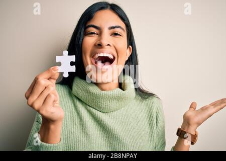 Jeune femme hispanique qui tient la pièce de puzzle comme solution de coopération sur les affaires très heureuse et excitée, expression gagnante célébrant la victoire Banque D'Images