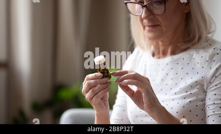 Une dame mûre ciblée qui examine l'étiquette de prescription de médicament à la maison. Banque D'Images