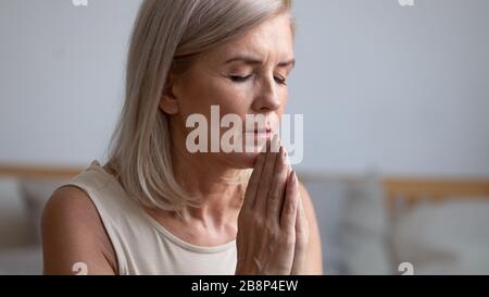 Femme mûre et fidèle focalisée priant avec des yeux fermés. Banque D'Images