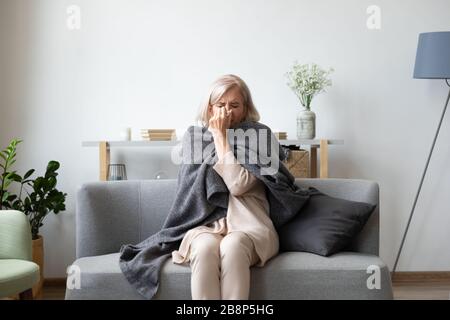 Femme malsaine d'âge moyen recouverte d'une couverture assise sur un canapé. Banque D'Images