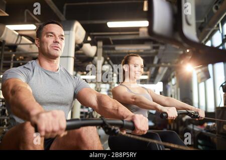 Vue en bas angle sur l'homme musculaire utilisant une machine d'exercice pendant l'entraînement de force dans la salle de sport moderne, espace de copie Banque D'Images