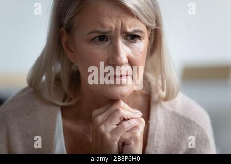 Frowning bouleverse la femme mûre assise seule, la tête a tourné vers le haut. Banque D'Images