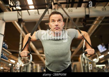 Portrait à faible angle de l'homme musculaire mûr faisant des pull-ups pendant l'entraînement de force dans la salle de sport moderne, espace de copie Banque D'Images