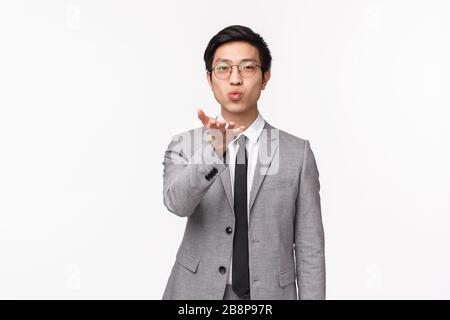 Portrait de taille-up romantique mignon, beau homme asiatique en costume gris, envoyer un baiser d'air à l'appareil photo, aller au bureau, dire acheter petite amie rester à la maison Banque D'Images