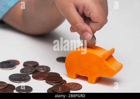 Une clôture de la main d'un enfant mettant une variété de pièces de monnaie ou de l'argent de l'allocation dans une très petite banque de porc. Banque D'Images