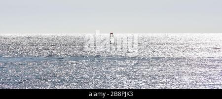 Le windsurfer furasant une mer d'argent par les réflexions du soleil Banque D'Images