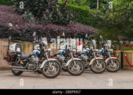 Chongqing, Chine - 9 mai 2010 : centre-ville. Gros plan de 4 motos de police identiques garées avec feuillage rouge et vert à l'arrière. Banque D'Images