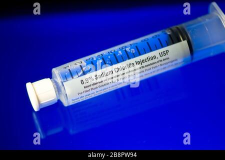 Gros plan du flacon d'injection de solution saline stérile pré-rempli sur une surface réfléchissante bleue. Banque D'Images
